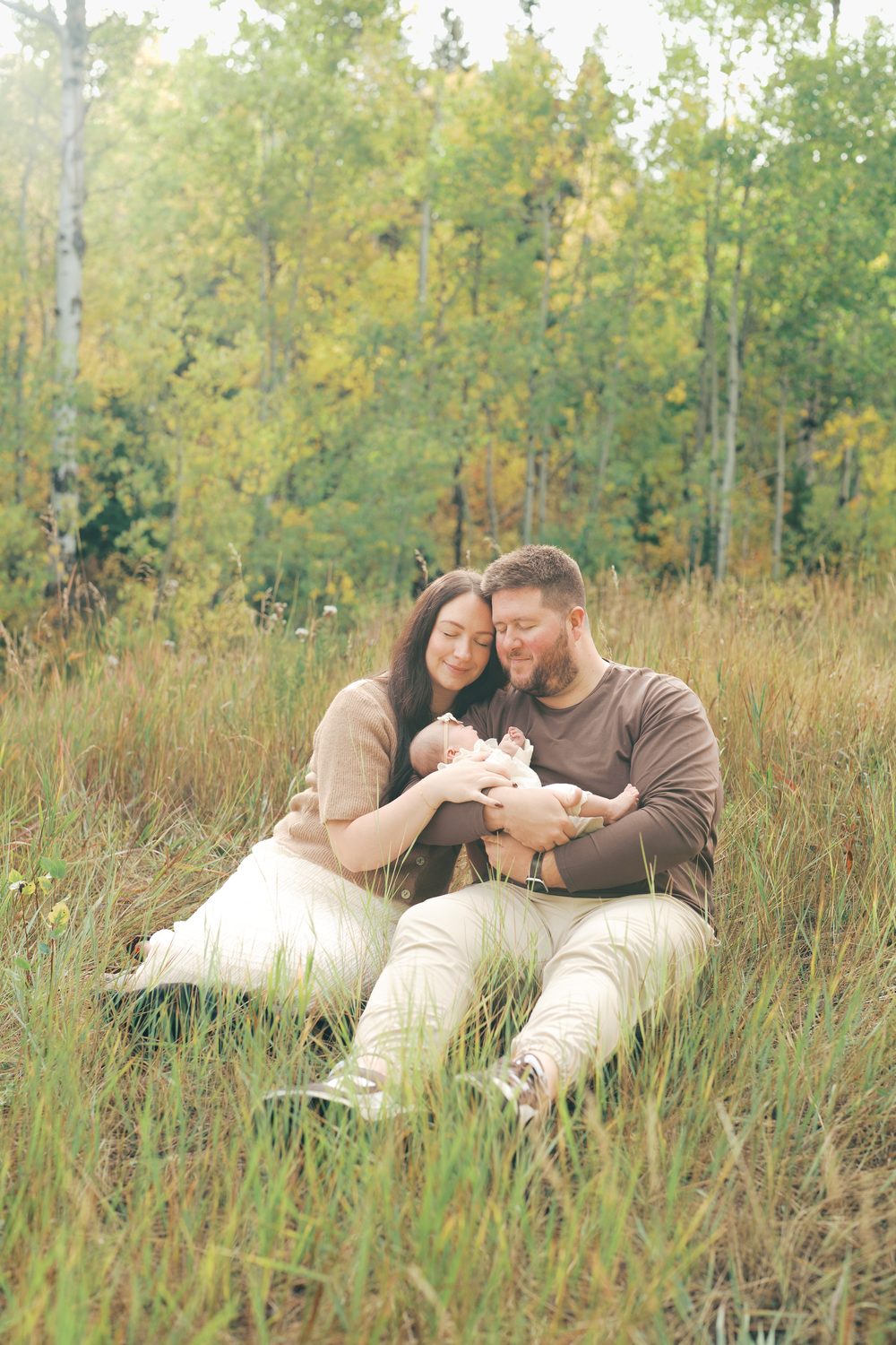 New parents cradling their baby girl in a golden aspen meadow