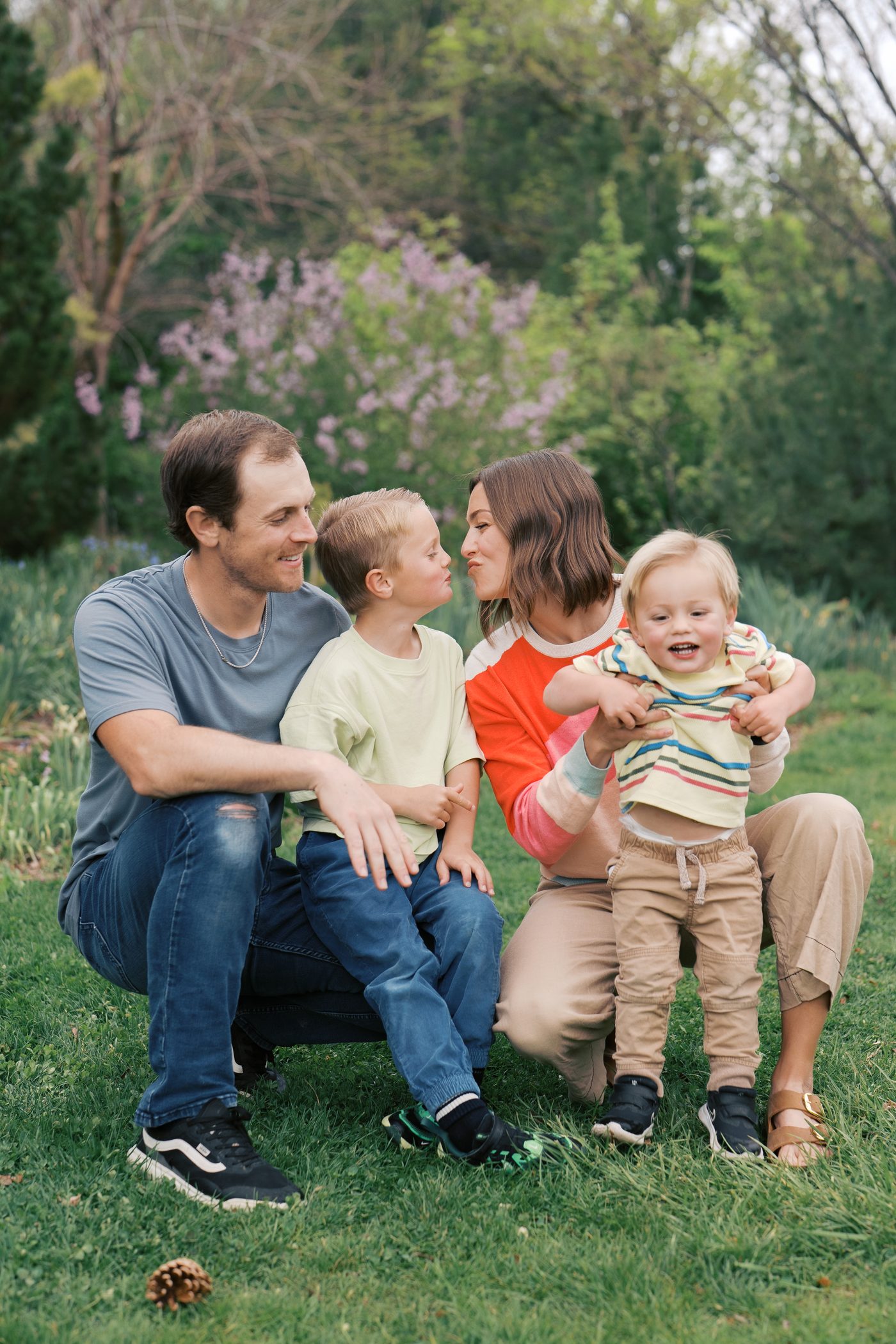 Mom kissing son on the nose while dad and toddler laugh in a spring Utah garden
