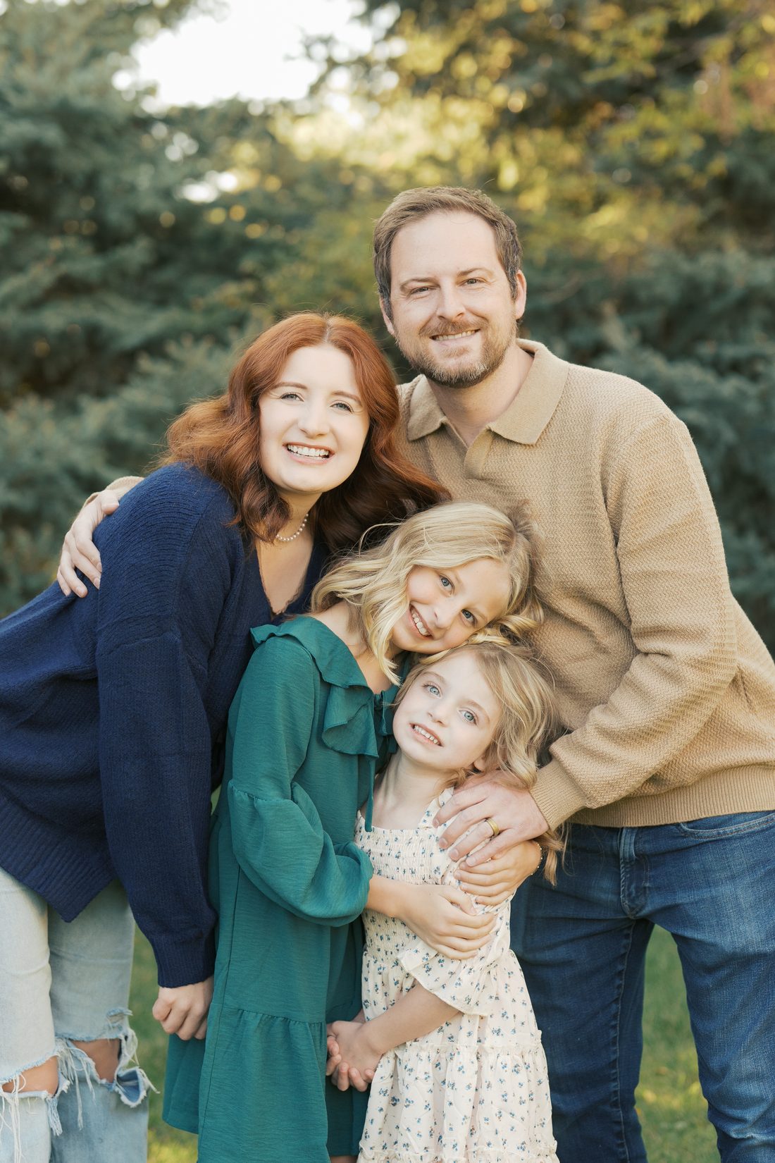 Mom, dad and two daughters hugging tight and laughing at golden hour