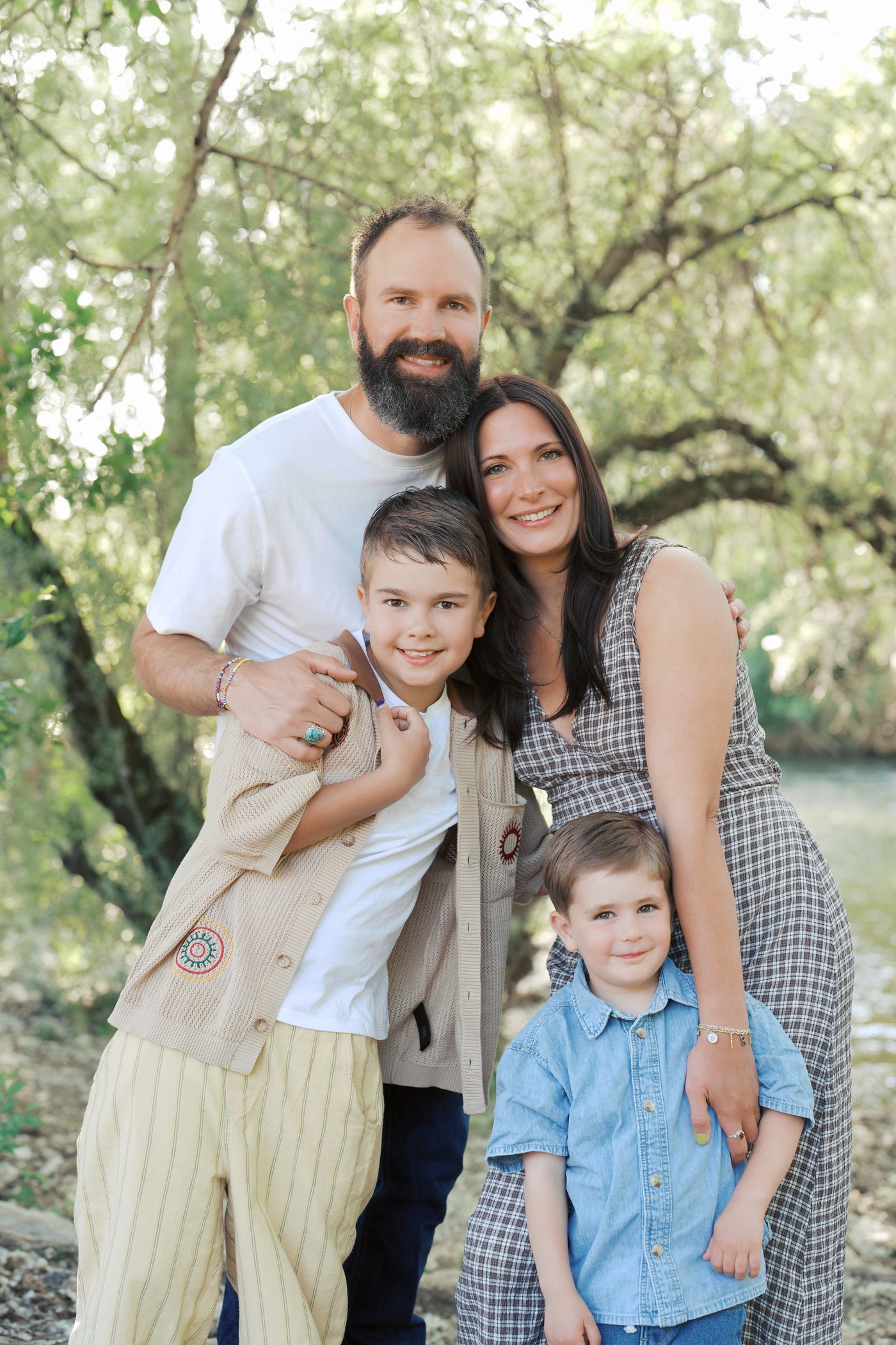 Family of four hugging under willow trees by a Utah creek