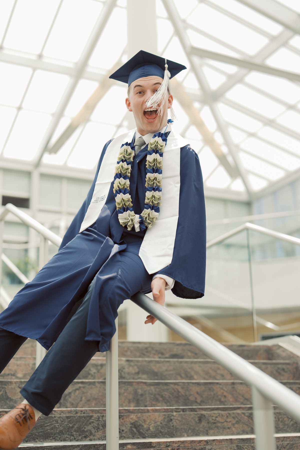 BYU graduate in cap and gown cheering on a staircase with a money lei