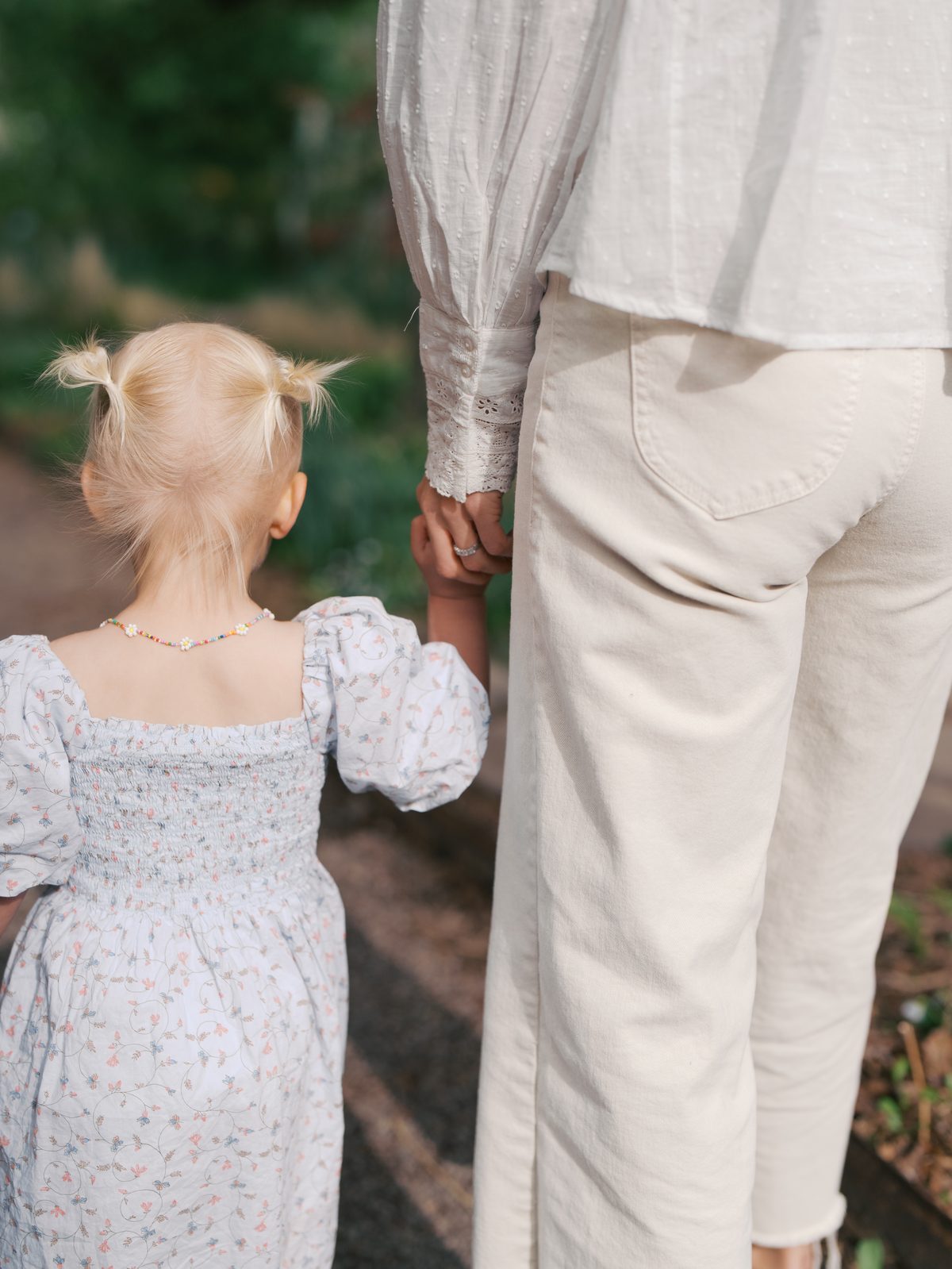 Toddler with pigtails holding her mom's hand in the garden