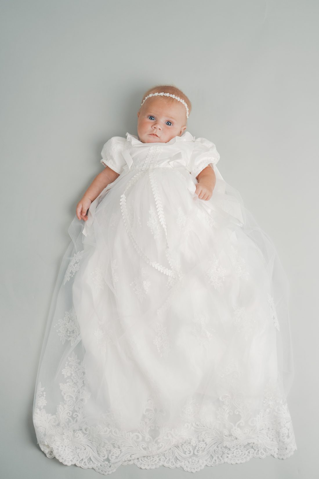 Baby girl in a white lace blessing gown looking up at the camera