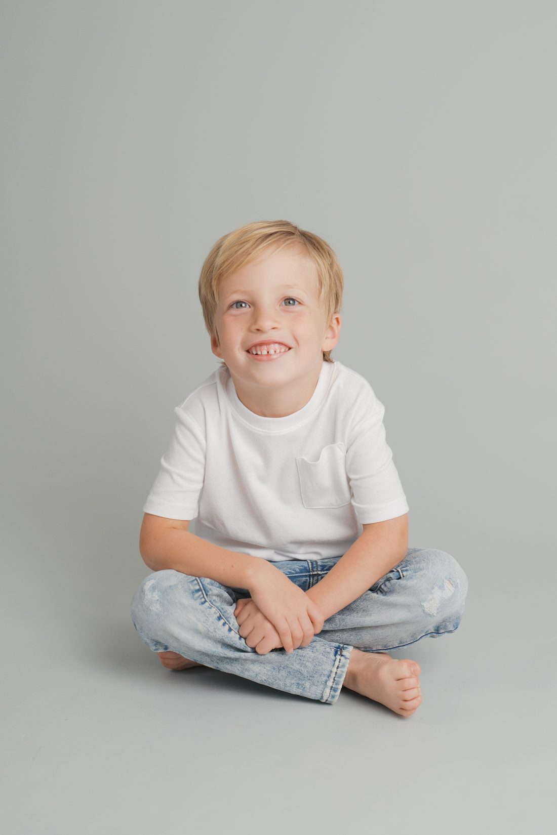 Barefoot boy in a white tee laughing cross-legged in the studio