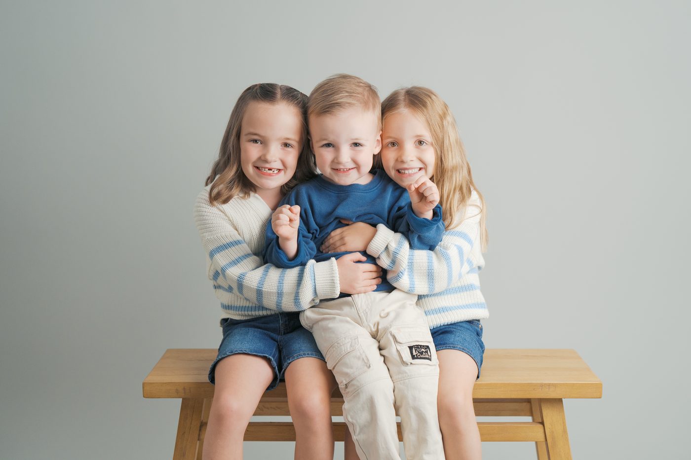 Three siblings hugging on a wooden bench in the studio