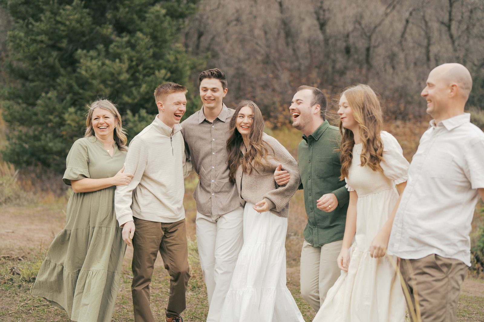 Big family laughing arm in arm while walking through a Utah canyon meadow