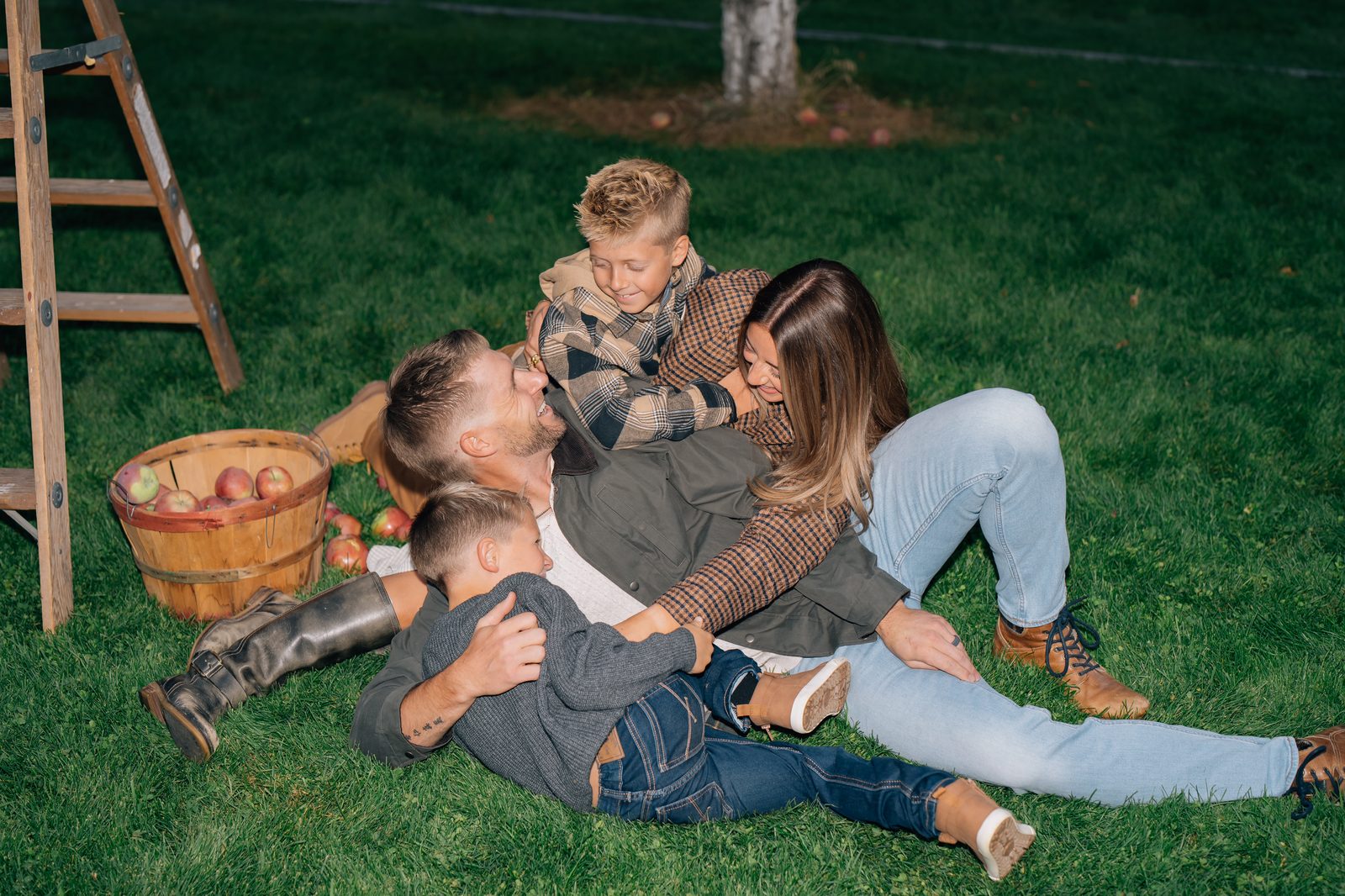 Family piled up laughing on the grass in a Utah apple orchard