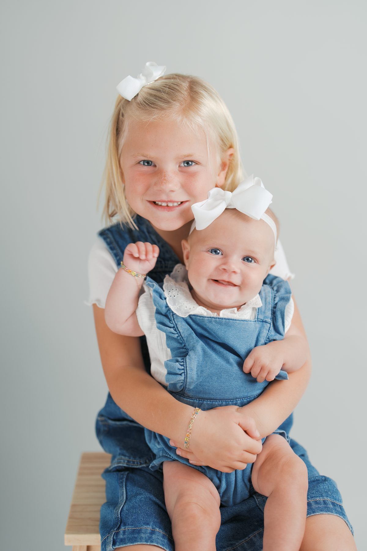 Big sister holding her smiling baby sister in the studio
