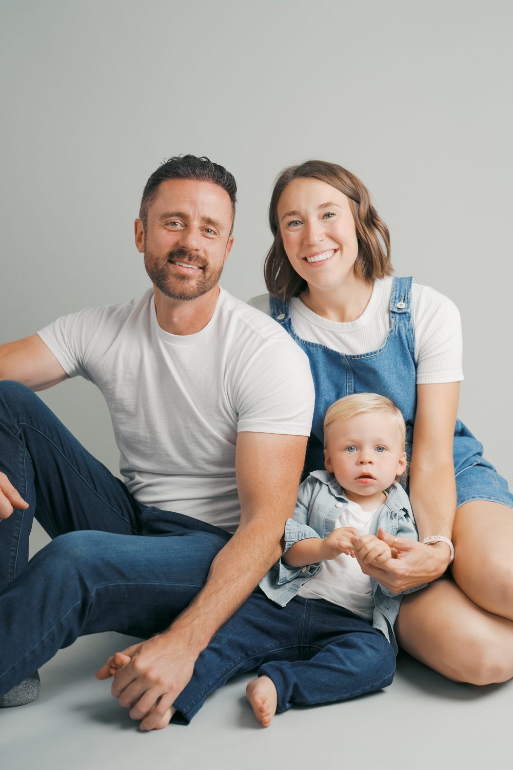 Parents sitting with their toddler in the studio on a soft gray backdrop